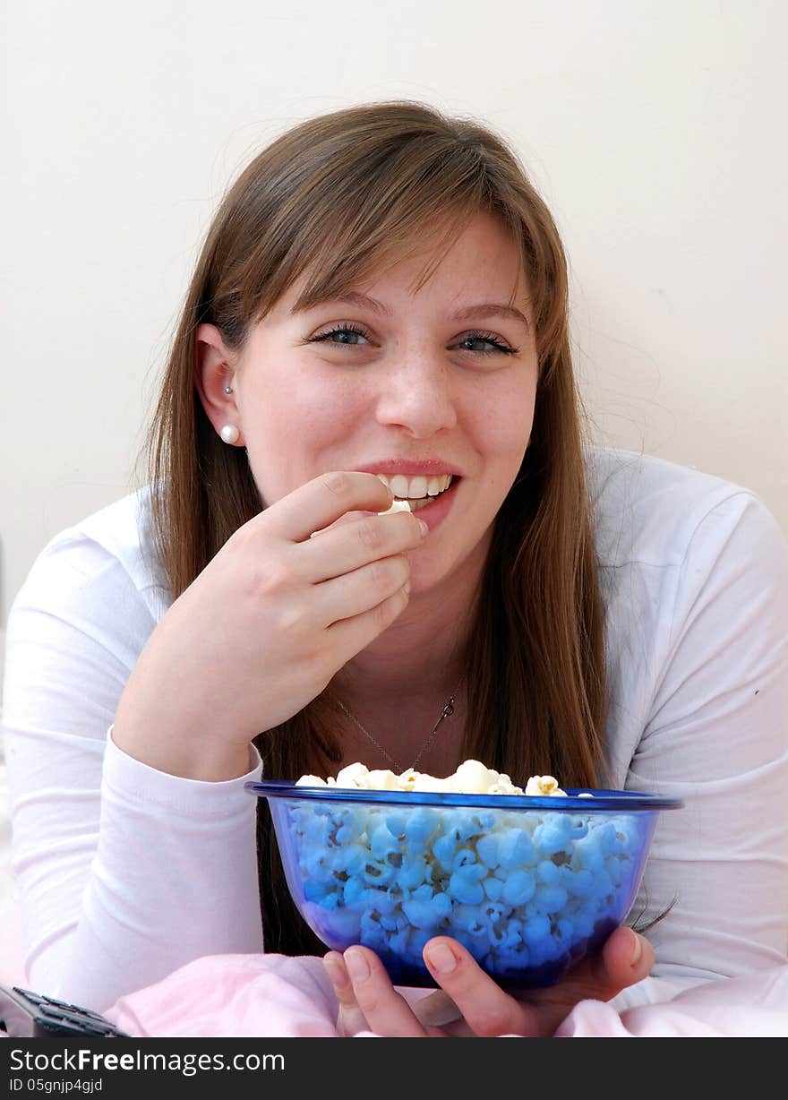 Beautiful young woman enjoying eating popcorn and talking on cell phone on her bed. Beautiful young woman enjoying eating popcorn and talking on cell phone on her bed.