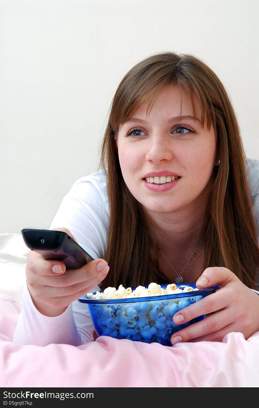 Beautiful young woman enjoying eating popcorn and holding tv control. Beautiful young woman enjoying eating popcorn and holding tv control.