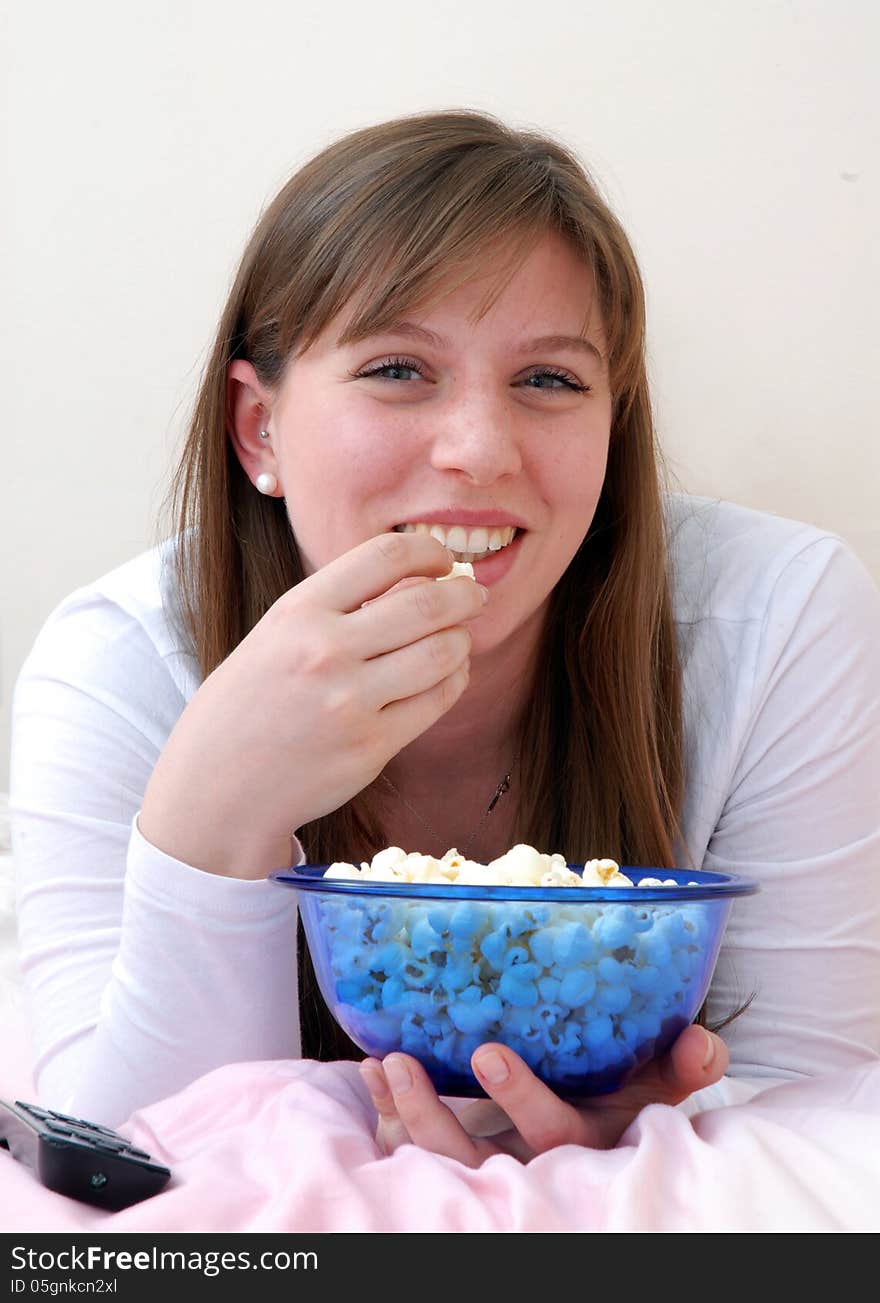 Beautiful young woman enjoying eating popcorn and talking on cell phone on her bed. Beautiful young woman enjoying eating popcorn and talking on cell phone on her bed