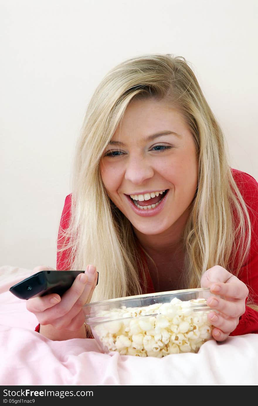 Beautiful young blonde woman enjoying eating popcorn on her bed. Beautiful young blonde woman enjoying eating popcorn on her bed