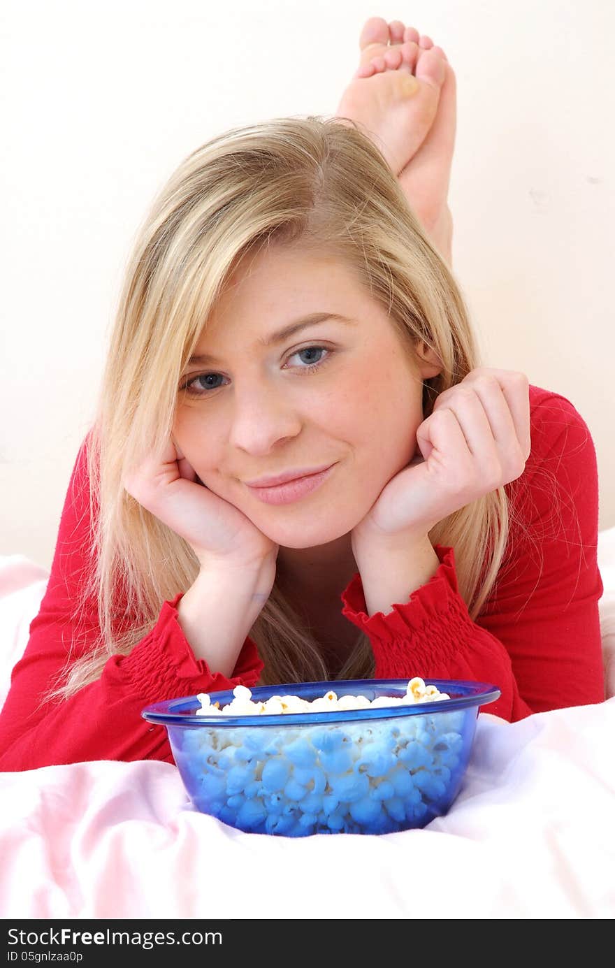 Beautiful young blonde woman enjoying eating popcorn on her bed. Beautiful young blonde woman enjoying eating popcorn on her bed.