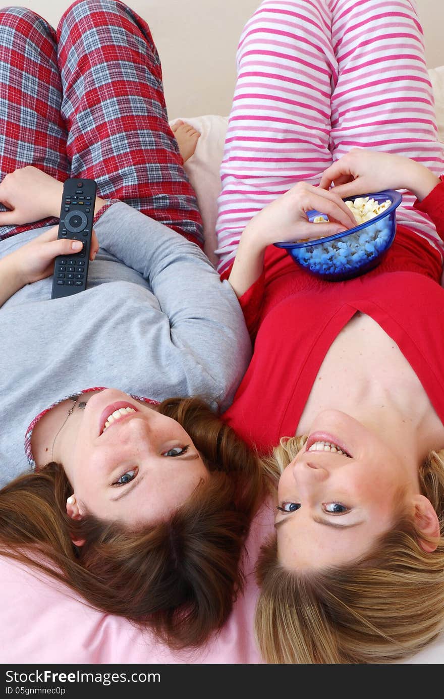 Two young women eating popcorn on bed. Two young women eating popcorn on bed