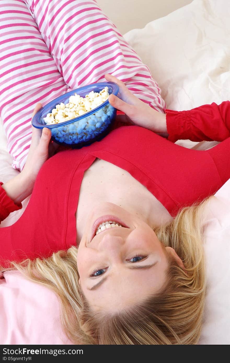 Beautiful young blonde woman enjoying eating popcorn on her bed. Beautiful young blonde woman enjoying eating popcorn on her bed