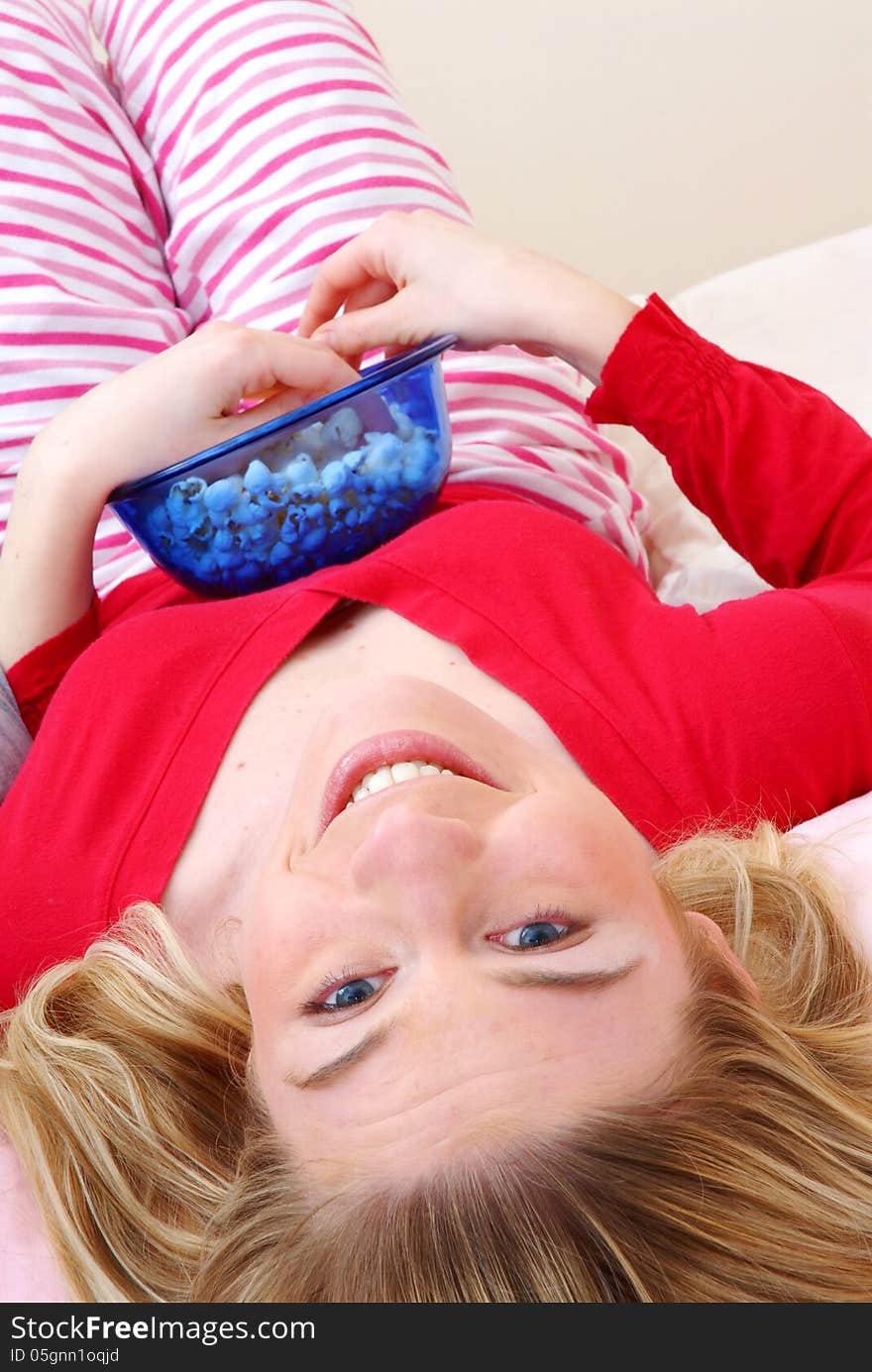 Beautiful young blonde woman enjoying eating popcorn on her bed. Beautiful young blonde woman enjoying eating popcorn on her bed