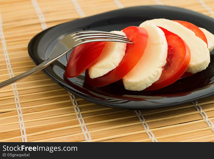 Tomato and mozzarella on black dish at bamboo