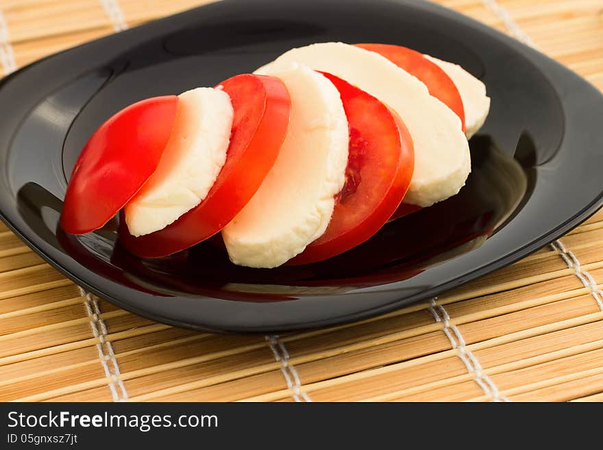 Tomato and mozzarella on black dish at bamboo background