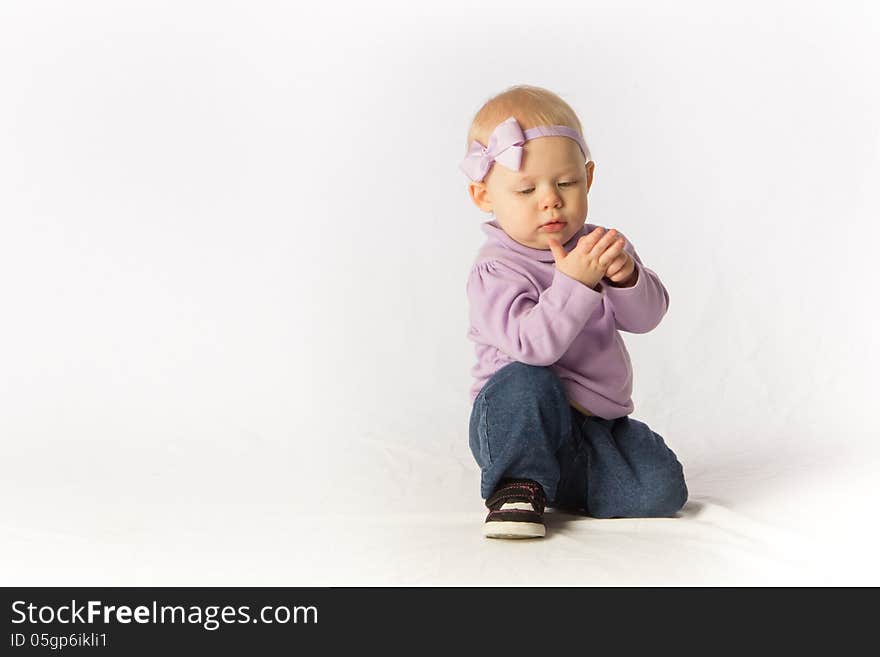 A baby girl kneels and inspects her hand. A baby girl kneels and inspects her hand