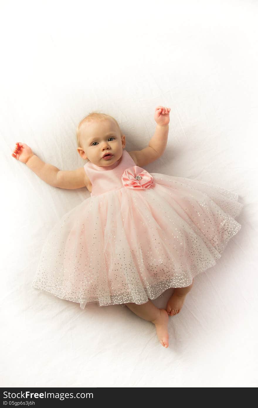 A serene little girl dressed in a pink frilly dress lays on a white background. A serene little girl dressed in a pink frilly dress lays on a white background