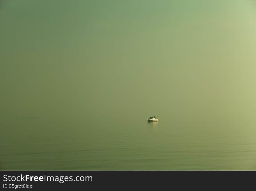 A motorboat lost in a green sea, with the mist that mixes water and sky.