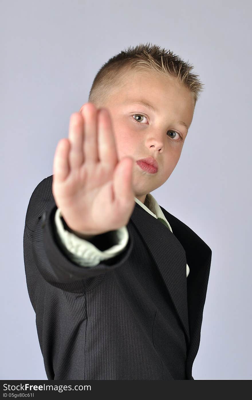 Young child in business suit with hand extended out to say stop on gray background. Young child in business suit with hand extended out to say stop on gray background