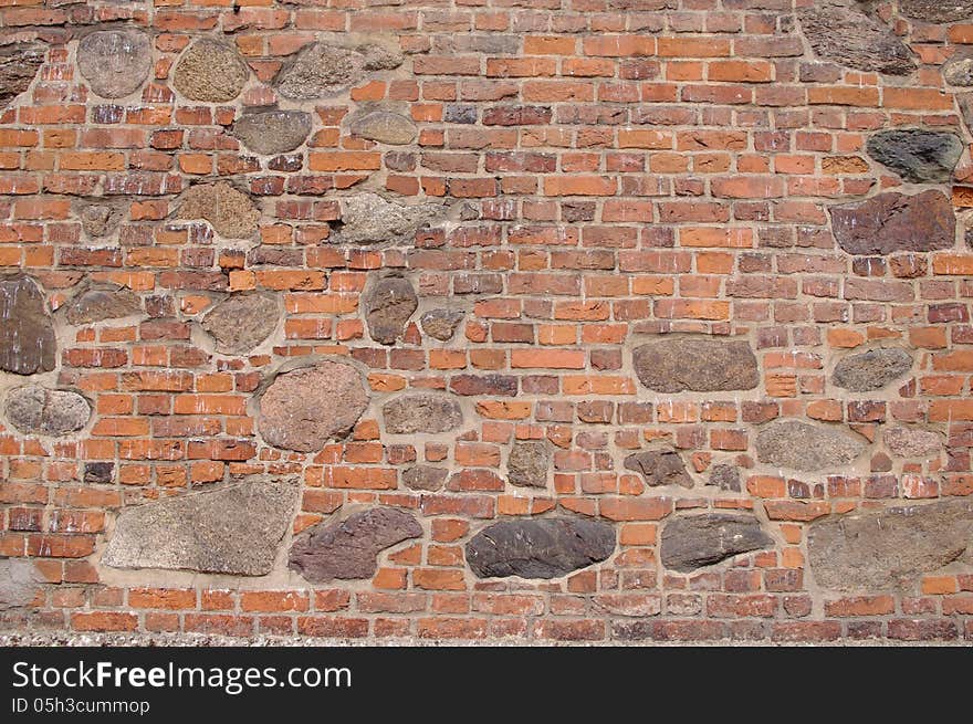 The photograph shows a wall, which is a fragment of an old church. It is made of bricks and large boulders of stone. The photograph shows a wall, which is a fragment of an old church. It is made of bricks and large boulders of stone.