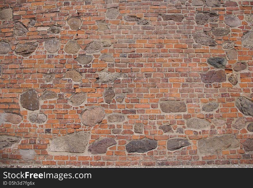 The photograph shows a wall, which is a fragment of an old church. It is made of bricks and large boulders of stone. The photograph shows a wall, which is a fragment of an old church. It is made of bricks and large boulders of stone.