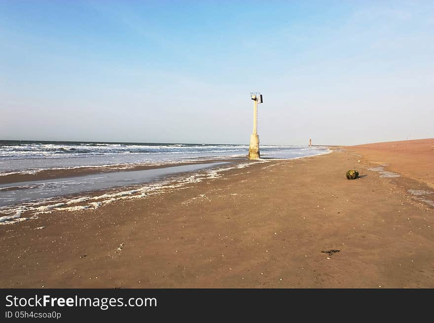 A long beach with a buoy, and a lightouse in distance. A long beach with a buoy, and a lightouse in distance