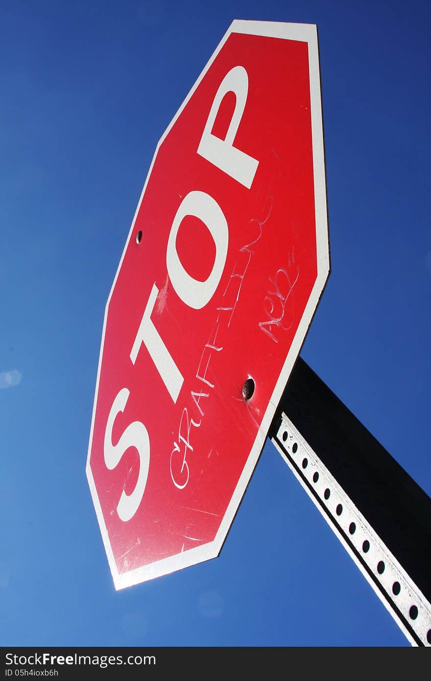 Stop sign with graffiti on it, against a clear blue sky.