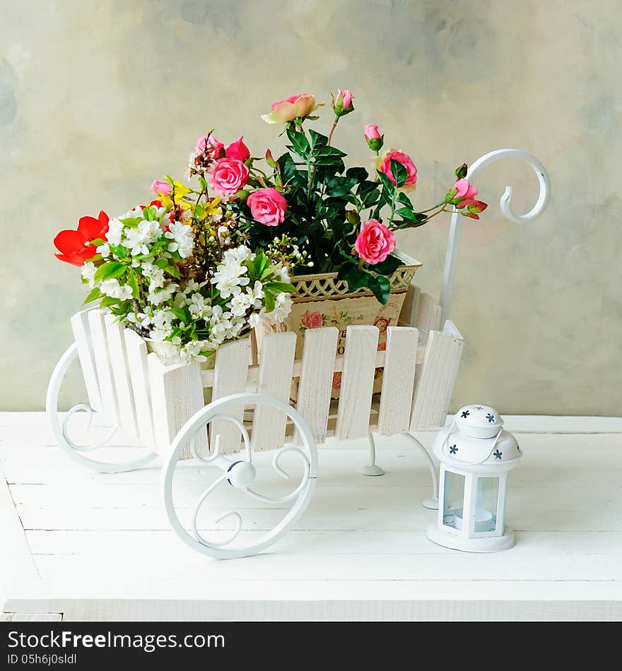 Decorative wheelbarrow with bright flowers in it and white lantern. Decorative wheelbarrow with bright flowers in it and white lantern