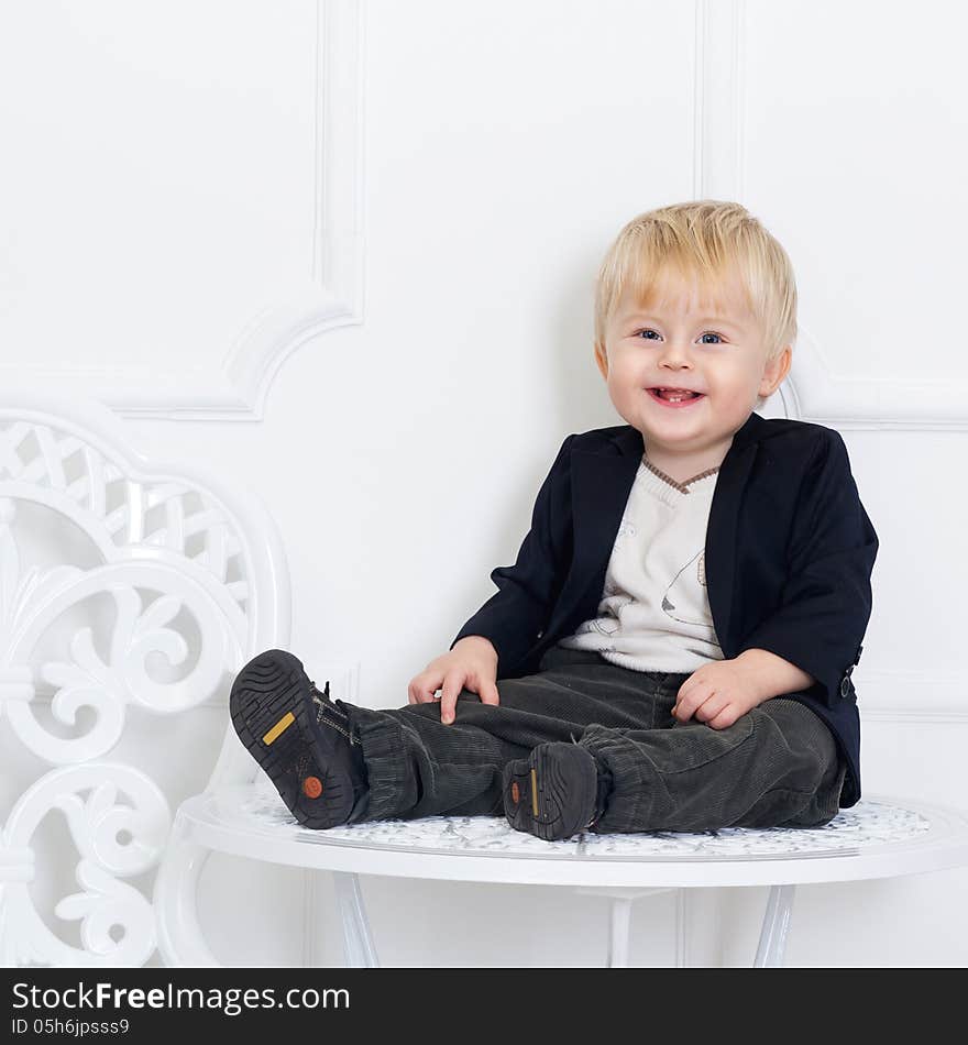 Positive kid in black jacket sitting on the table on white. Positive kid in black jacket sitting on the table on white