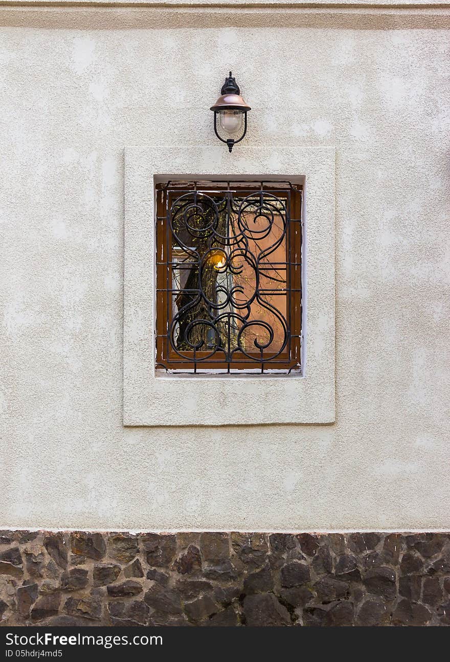 Window with wrought protection and a lantern on the wall with a stone basement. Window with wrought protection and a lantern on the wall with a stone basement