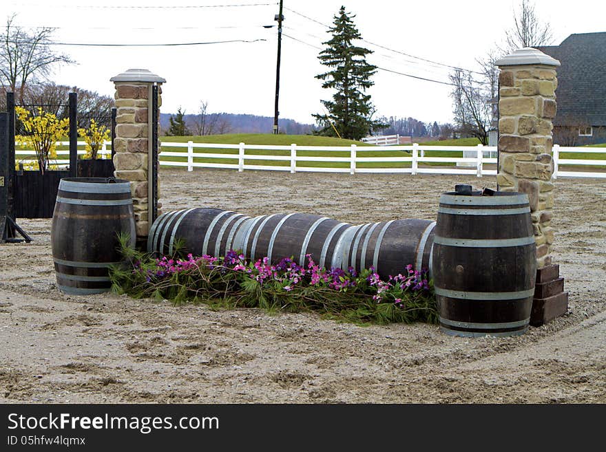 Horse jump consisting of two stone pillars and lengthwise barrels decorated with greenery and pink flowers. Horse jump consisting of two stone pillars and lengthwise barrels decorated with greenery and pink flowers.