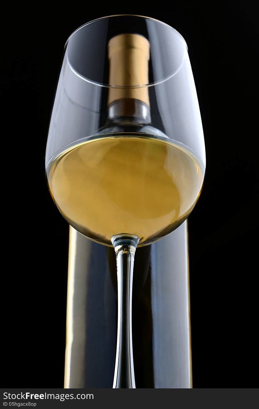 A glass of white wine and wine bottle on black.