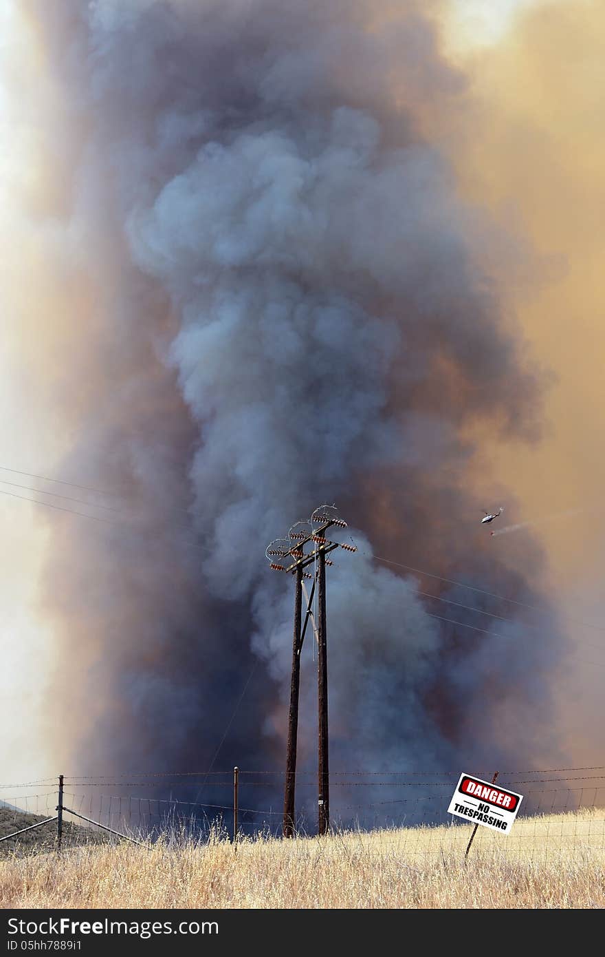 Out of control brush fire with water dropping helicopter and danger sign.