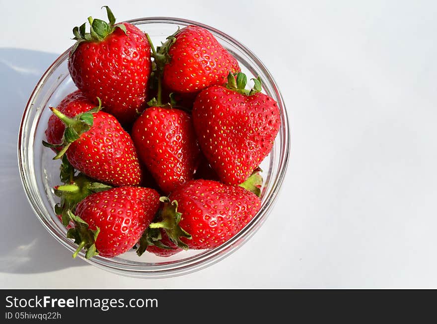 Strawberries in glass bowl in sunlight, with shadow, over white background. Strawberries in glass bowl in sunlight, with shadow, over white background