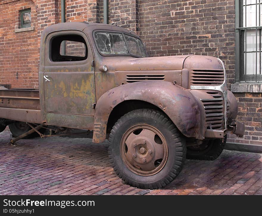 Front part of an old rusty truck with a broken windshield in a brick alleyway next to a brick wall. Front part of an old rusty truck with a broken windshield in a brick alleyway next to a brick wall.