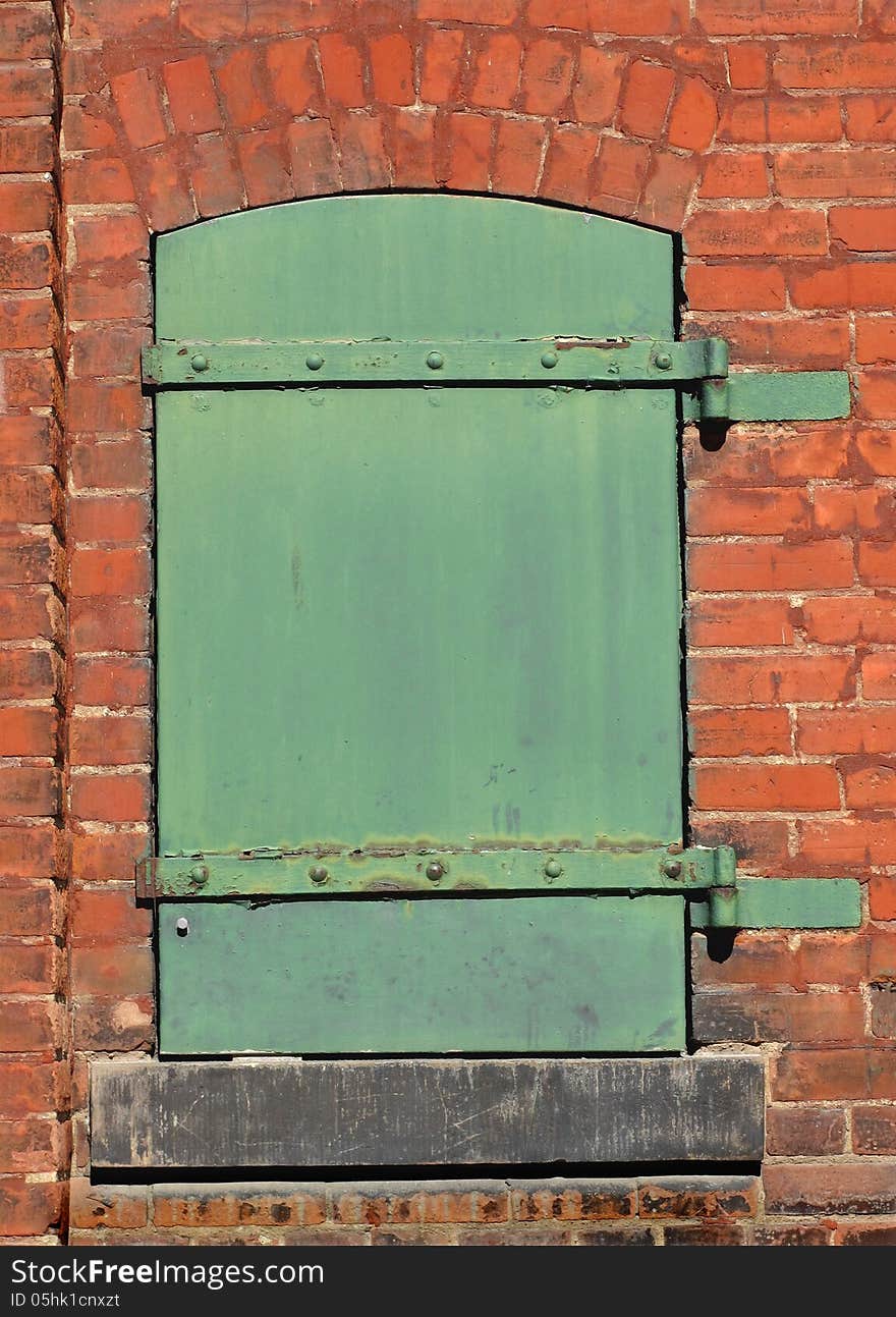 Old, worn, and weathered small closed green solid metal door in the brick wall of an old factory. Old, worn, and weathered small closed green solid metal door in the brick wall of an old factory