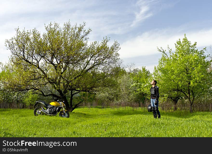 Biker with a sport motorbike resting against a nature calm landscape with a blue cloudy sky and breathes a scent of a spring fresh air. Biker with a sport motorbike resting against a nature calm landscape with a blue cloudy sky and breathes a scent of a spring fresh air.