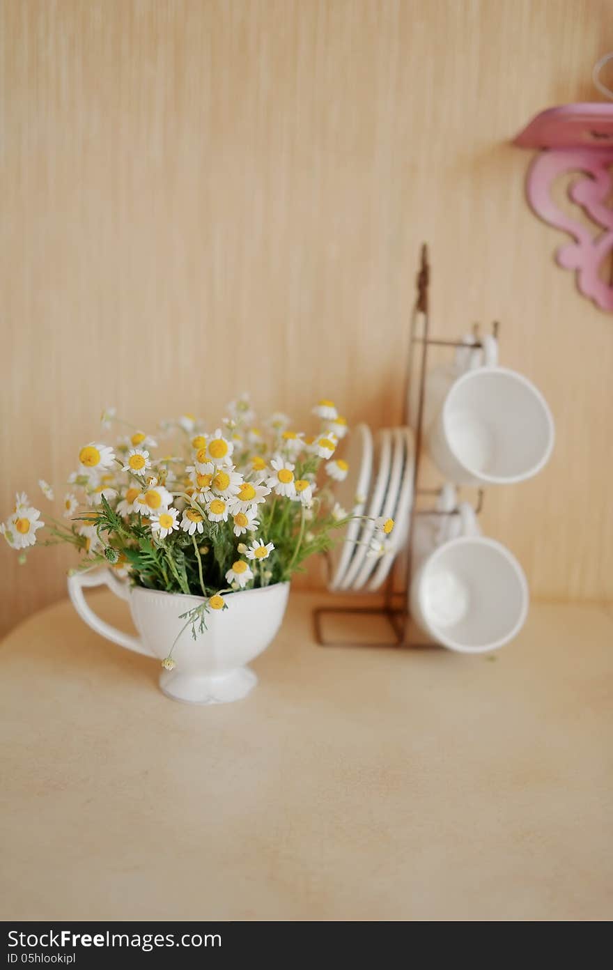 On a beige background white cup on a stand, and one with a bouquet of daisies. On a beige background white cup on a stand, and one with a bouquet of daisies