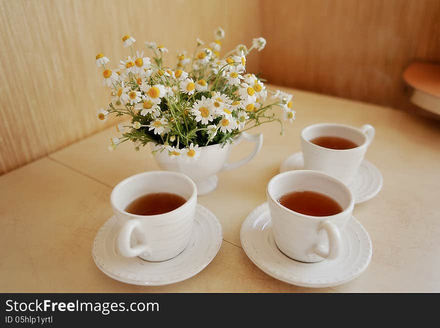 Beautiful table setting of white cups of tea and white vase bouquet of daisies. Beautiful table setting of white cups of tea and white vase bouquet of daisies