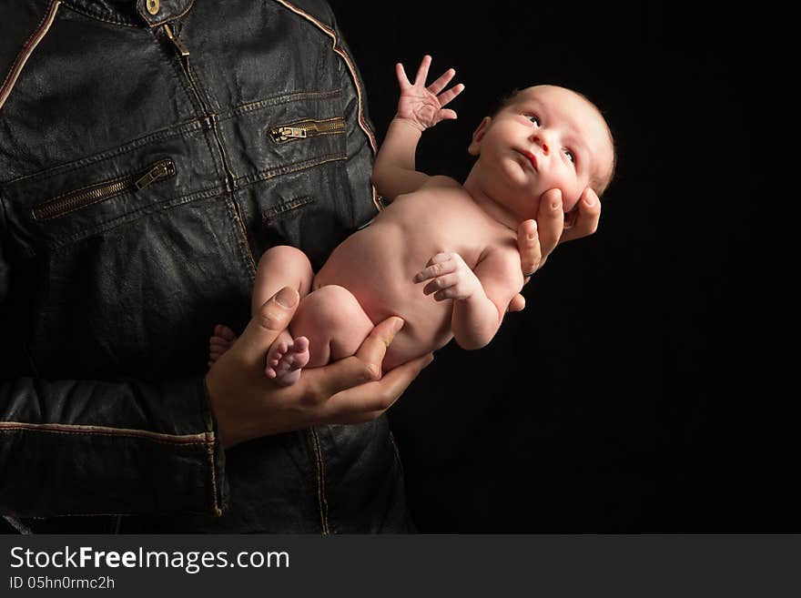 A father in a motorcyclist jacket holds his newborn son. A father in a motorcyclist jacket holds his newborn son