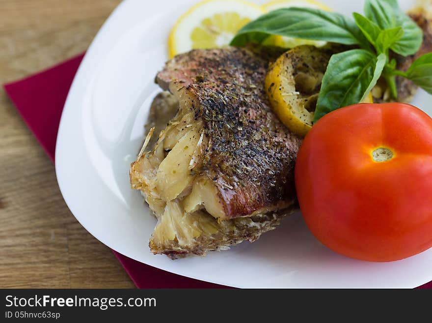 Baked grouper served with lemon and basil on white plate with tomato