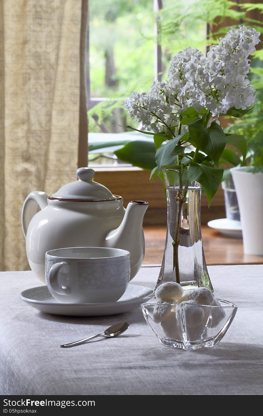 Teapot, teacup, sweets and white lilac in a glass vase. Teapot, teacup, sweets and white lilac in a glass vase