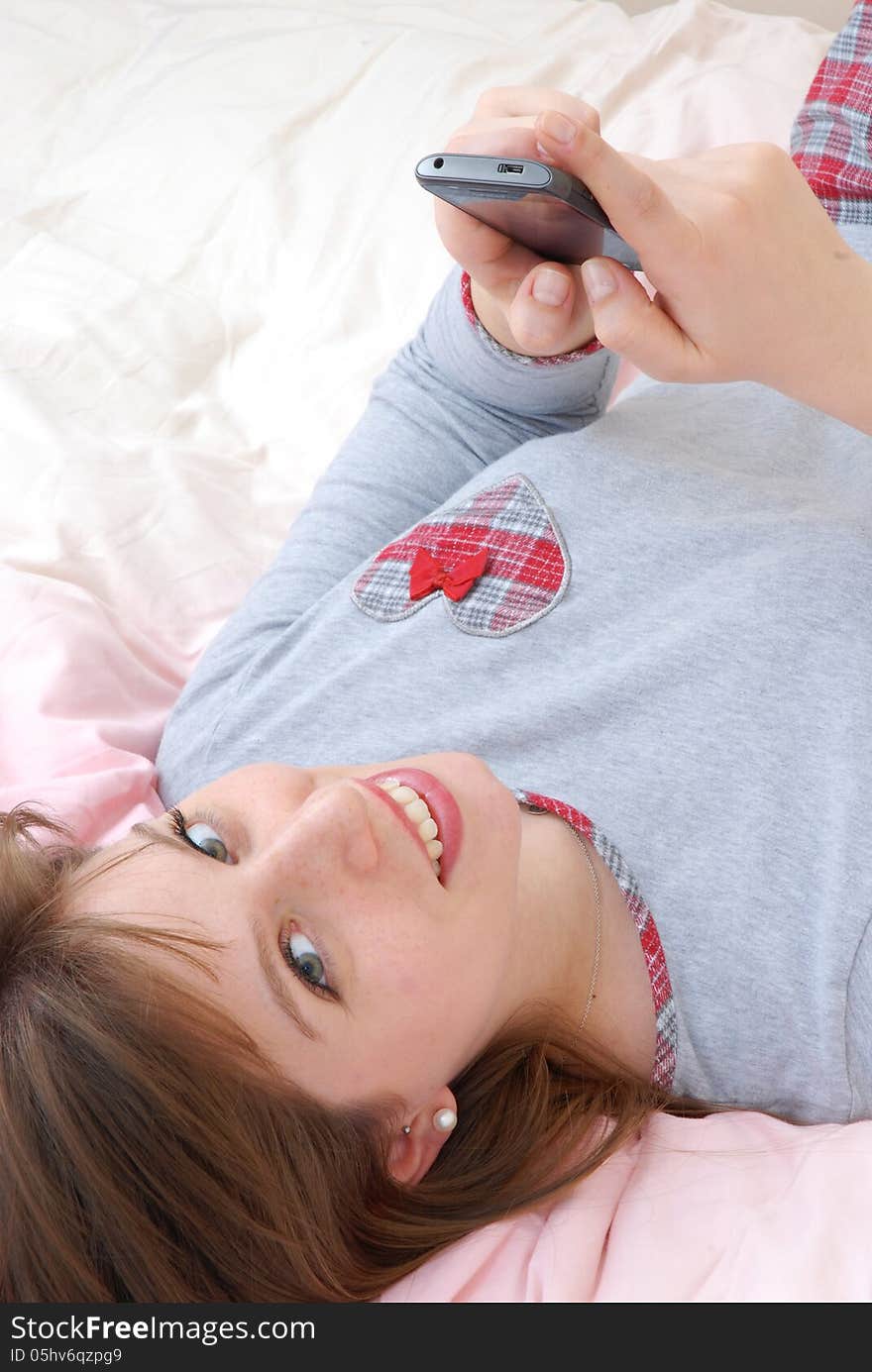 Young woman lying down on bed and sending cell phone text. Young woman lying down on bed and sending cell phone text.