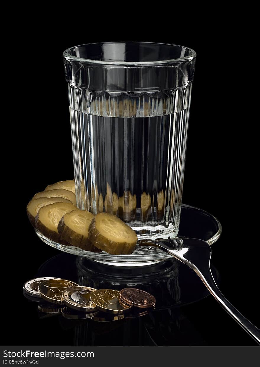 EURO coins near to a thick glass tumbler, a pickle and a fork on a saucer. EURO coins near to a thick glass tumbler, a pickle and a fork on a saucer.