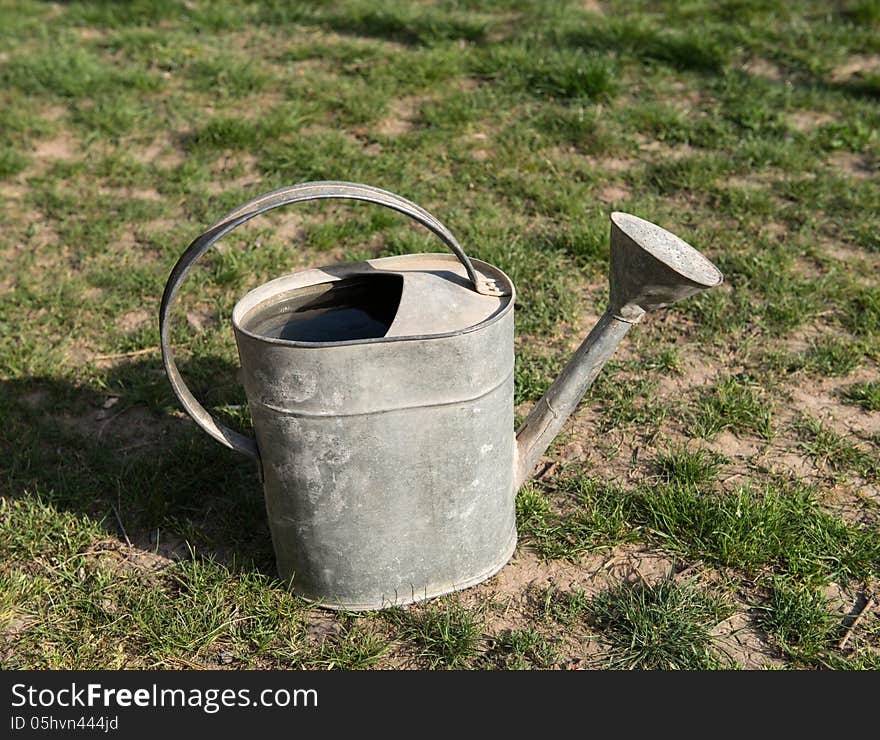 Aged metallic watering pot full of water on natural background.