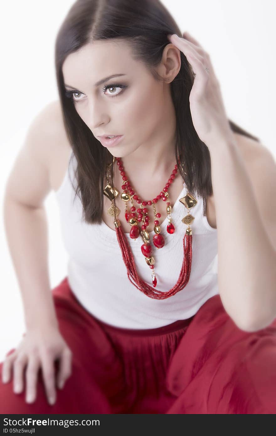 Portrait of young gorgeous woman wearing vivid necklace of red color beads. Dressed in red skirt and white t-shirt. Selective focus. Shot in studio. Over white background. Portrait of young gorgeous woman wearing vivid necklace of red color beads. Dressed in red skirt and white t-shirt. Selective focus. Shot in studio. Over white background.