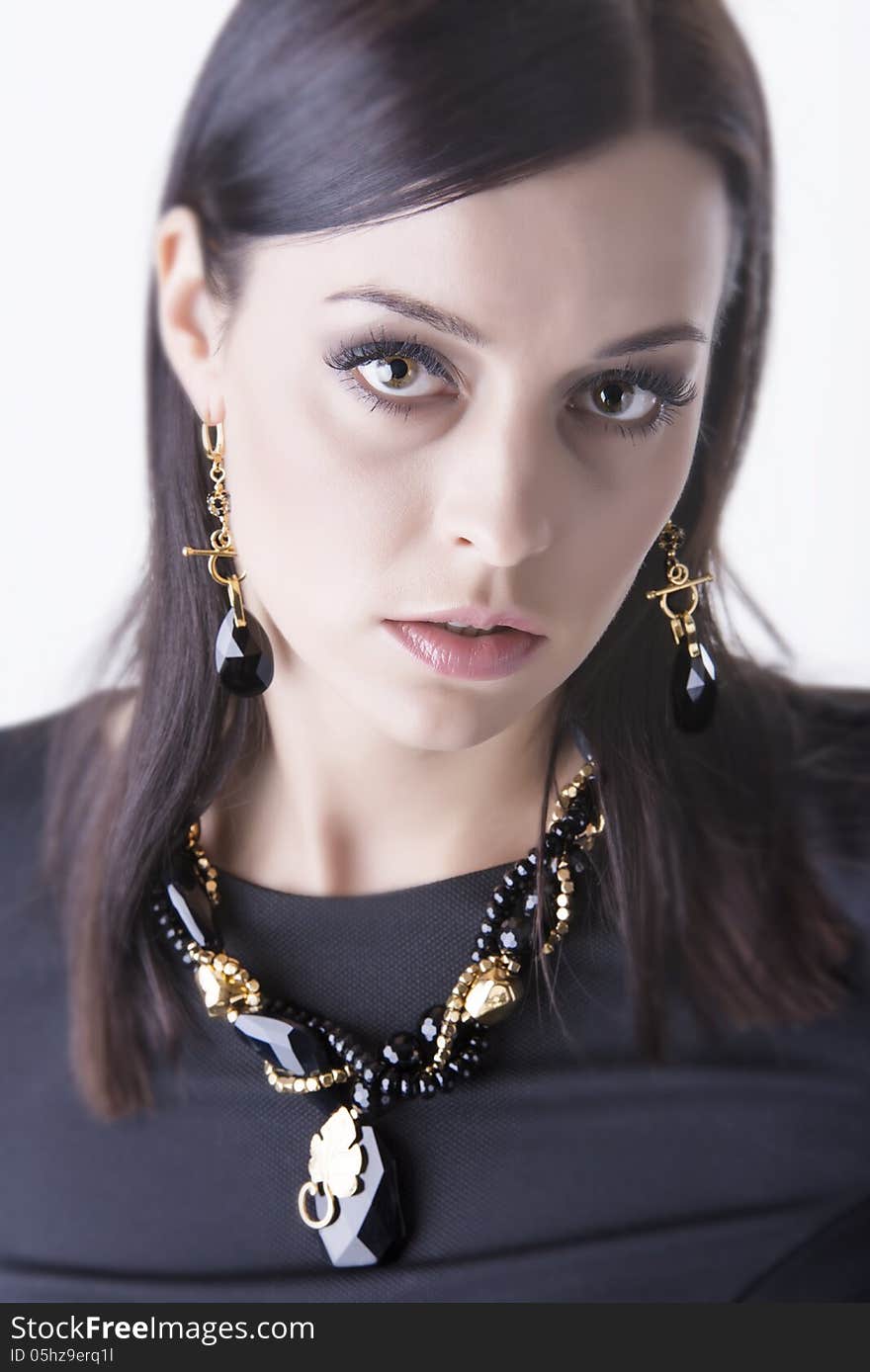 Close up portrait of young and beautiful glamour woman dressed in black cloth and wearing luxurious black stones jewelry- necklace and earrings, looking up straight to the camera. Shot in studio. Over white background. Close up portrait of young and beautiful glamour woman dressed in black cloth and wearing luxurious black stones jewelry- necklace and earrings, looking up straight to the camera. Shot in studio. Over white background.