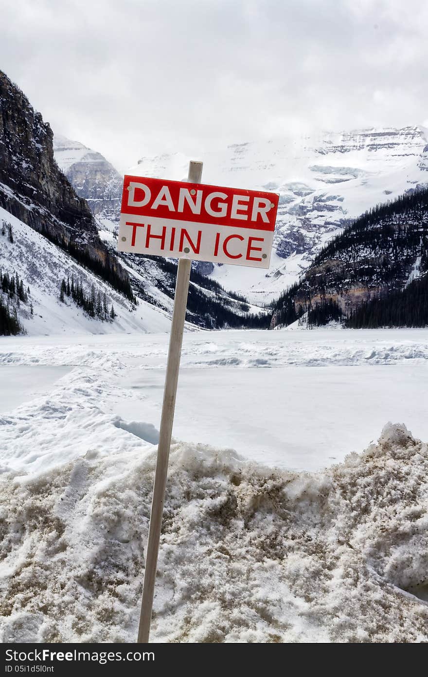 Danger thin ice sign with Canadian rockies and the frozen Lake Louise in the background
