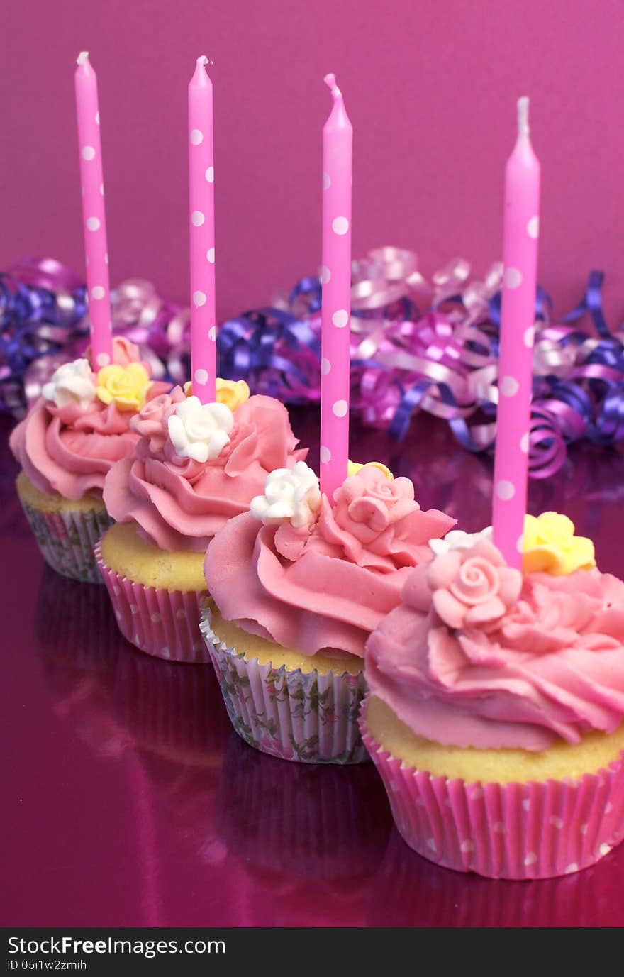 Pink brithday cupcakes with polka dot candles against a pink background. Vertical with shallow focus on second cupcake. Pink brithday cupcakes with polka dot candles against a pink background. Vertical with shallow focus on second cupcake.