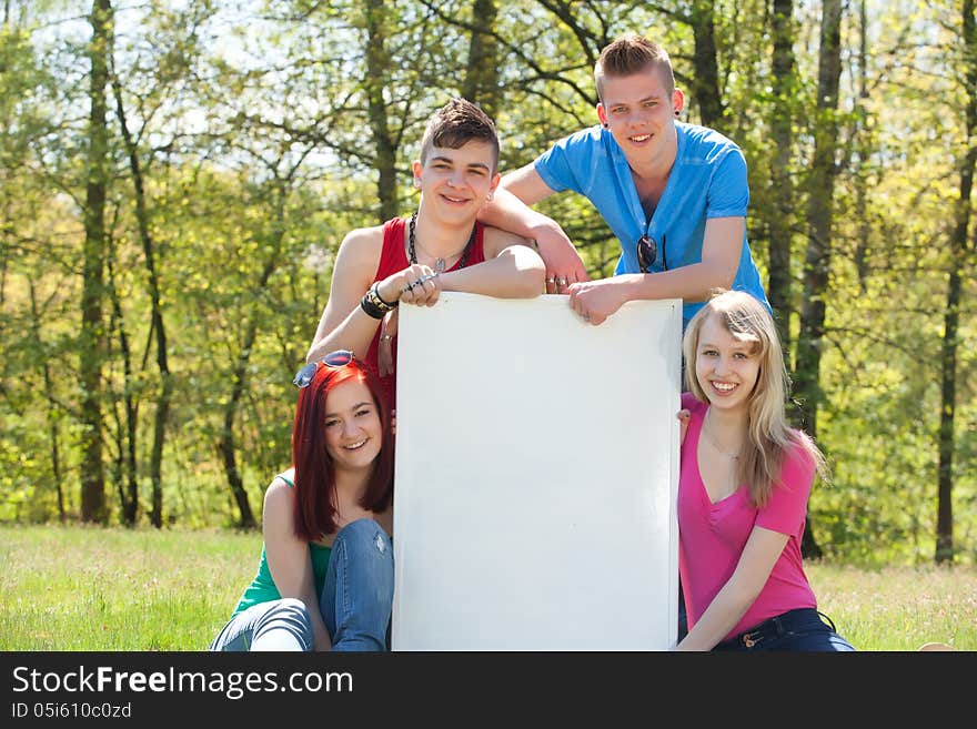 Four teenagers in colored shirts and a white board which can be used for your advertisements. Four teenagers in colored shirts and a white board which can be used for your advertisements