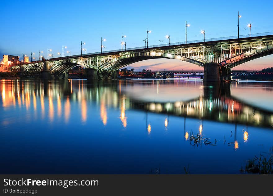 Backlit bridge at night and reflected in the water