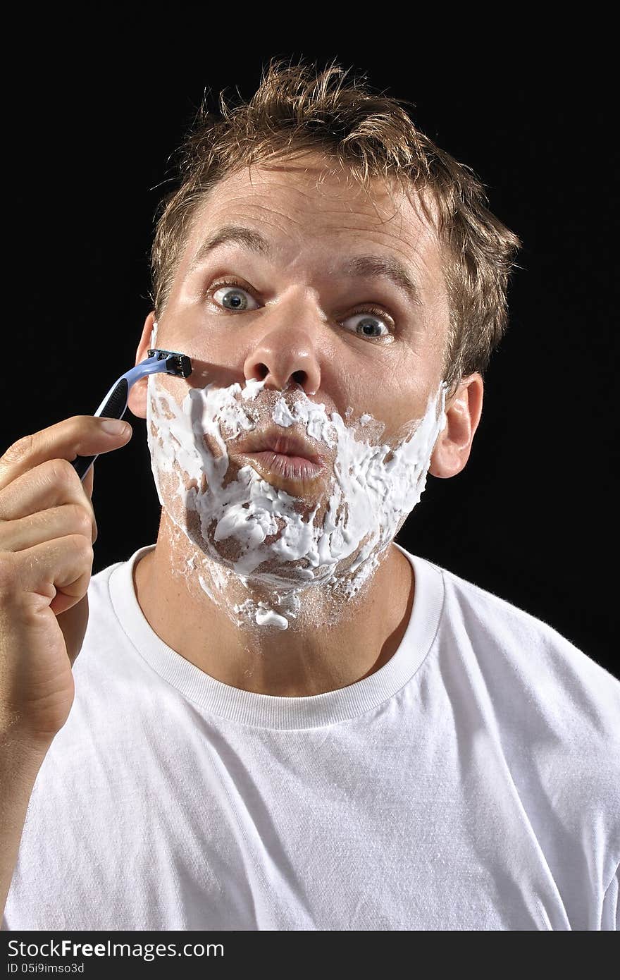 Handsome Caucasian man with messy bed head hair makes funny face while shaving his cheek on black background. Handsome Caucasian man with messy bed head hair makes funny face while shaving his cheek on black background