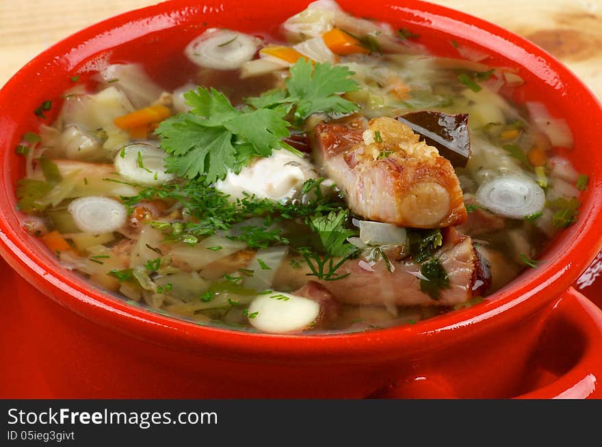 Delicious Vegetable Soup with Smoked Pork Ribs, Cabbage, Leek, Carrot, Garlic and Greens in Red Bowl closeup