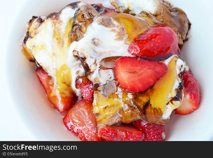 Close up of chopped strawberries with ice cream and black, pine honey in porcelain bowl, view from above. Close up of chopped strawberries with ice cream and black, pine honey in porcelain bowl, view from above