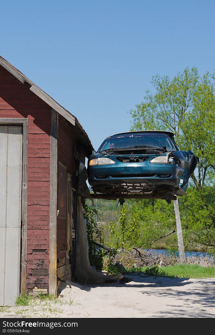 Old beat up Ford Mustang hanging in the air off the side of a garage. Old beat up Ford Mustang hanging in the air off the side of a garage.