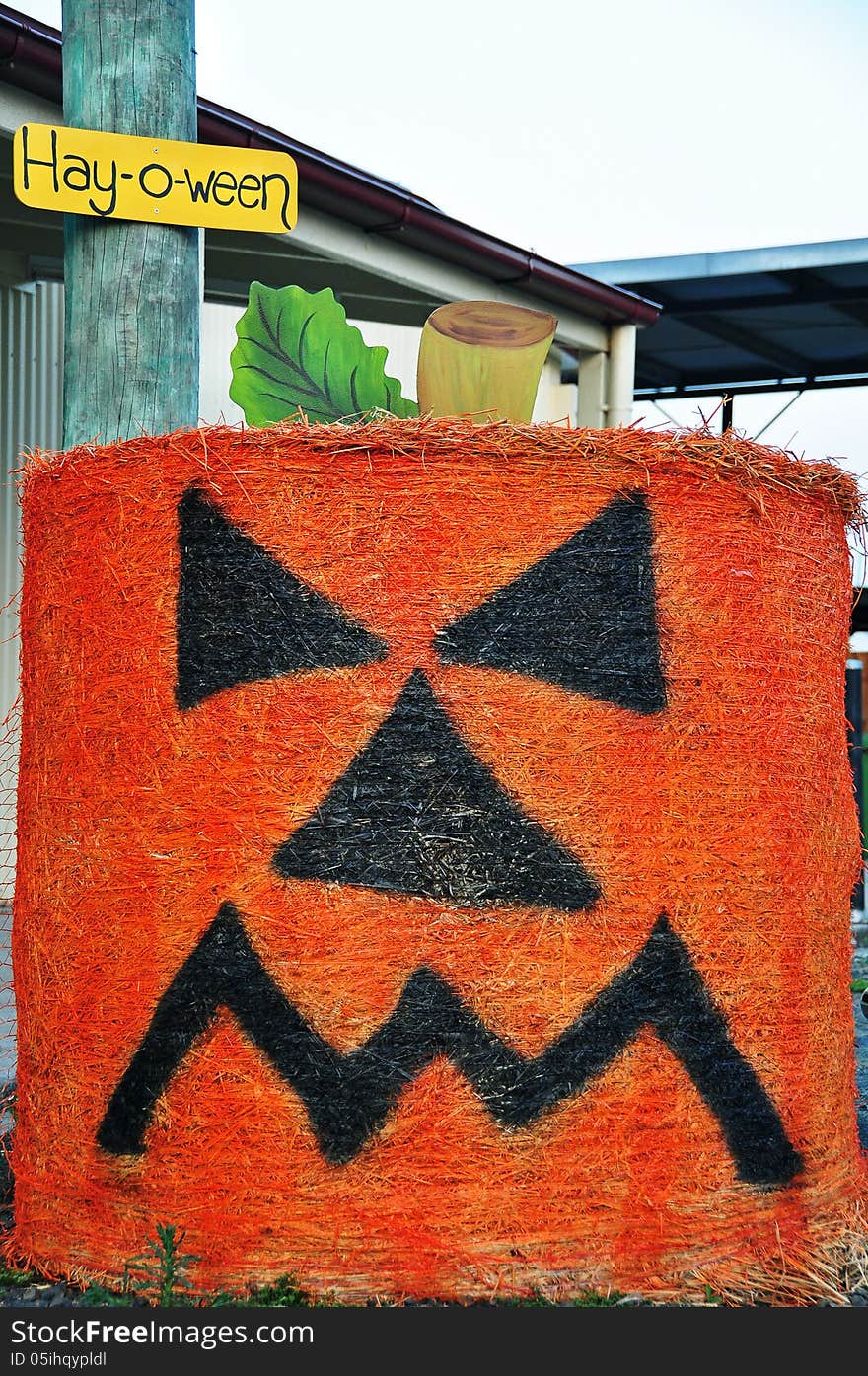 A comical and creative large roadside halloween painted hay bale with the cranky expression of an orange pumpkin on the front and a sign Hay-o-ween. A comical and creative large roadside halloween painted hay bale with the cranky expression of an orange pumpkin on the front and a sign Hay-o-ween.