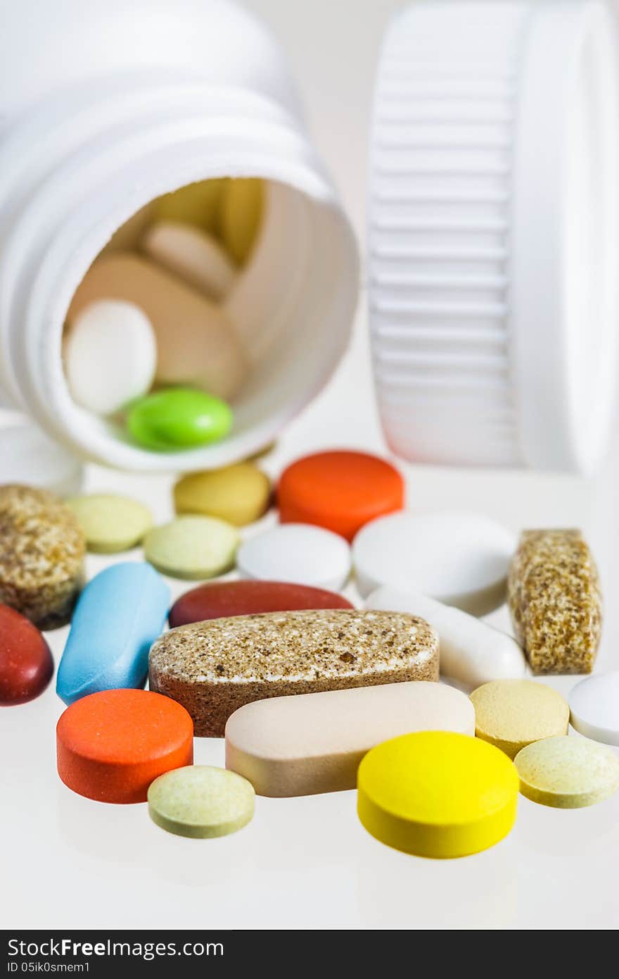 Various colorful pills scattered from white bottle on white background