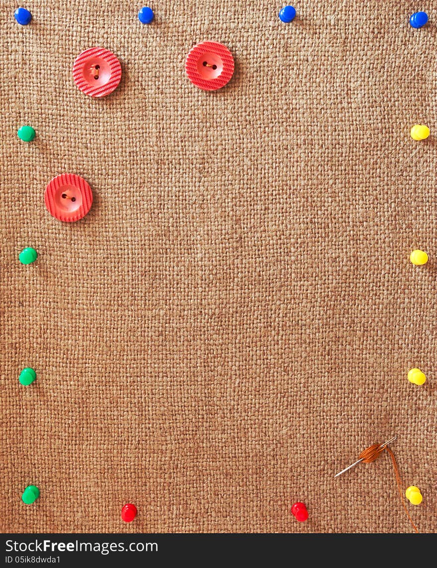 Burlap background decorated with variegated pins, buttons and needle. Burlap background decorated with variegated pins, buttons and needle