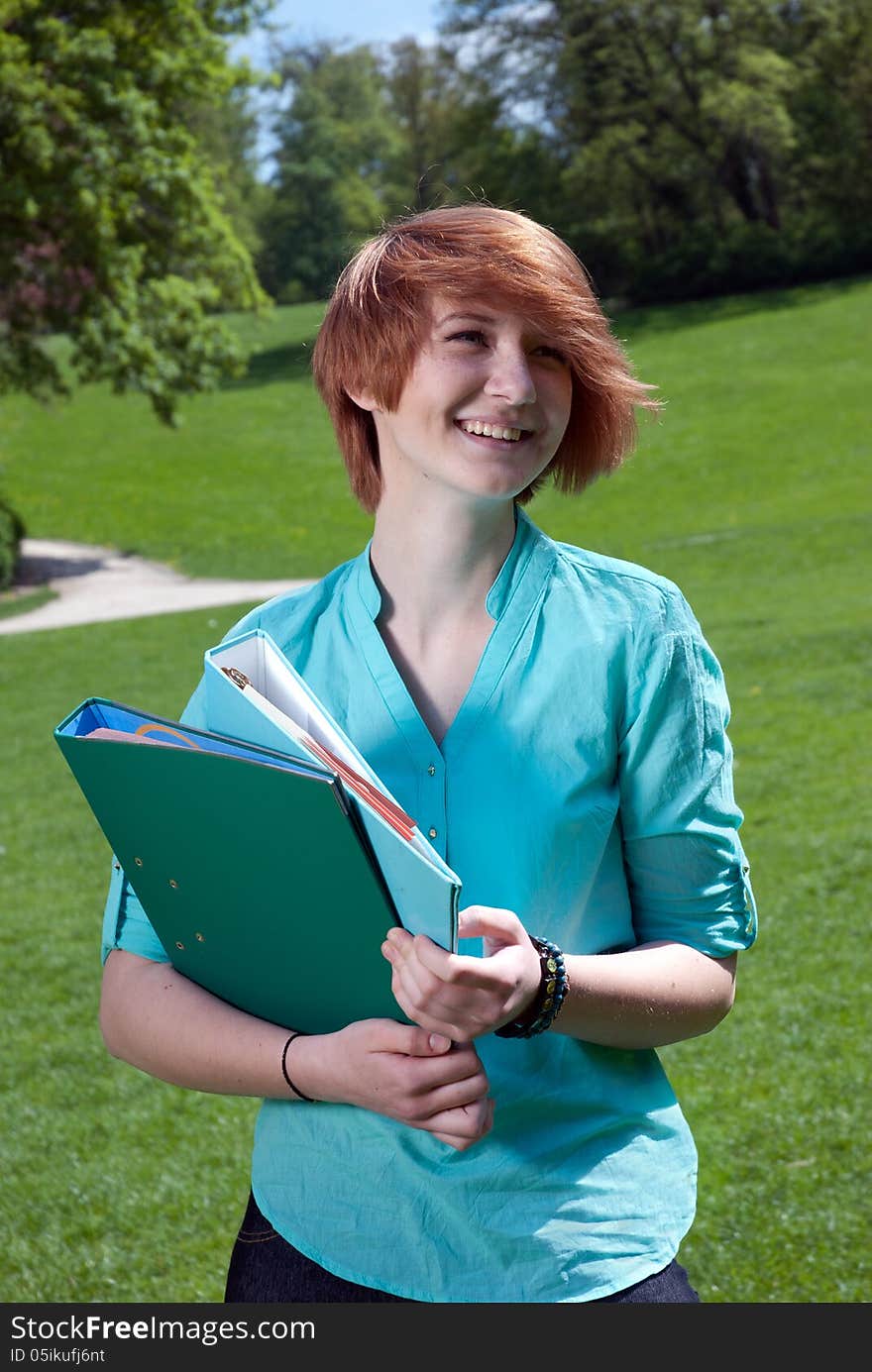 Smiling young woman holding a file folder in a park. Smiling young woman holding a file folder in a park